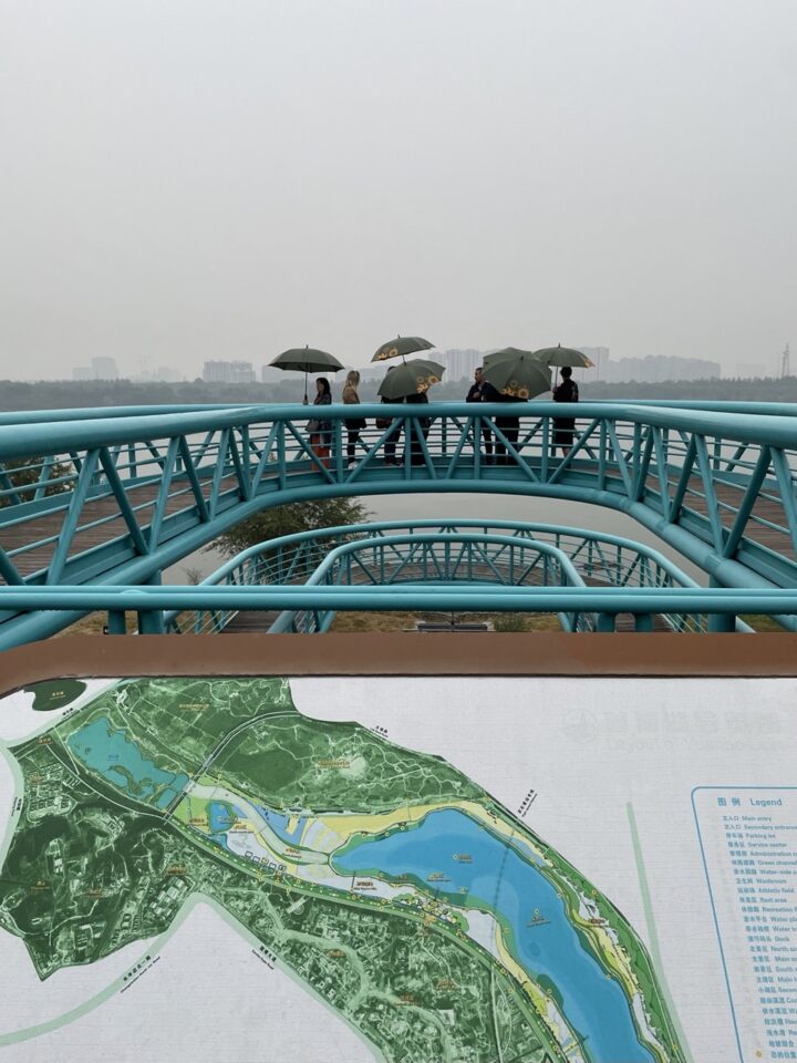 Signage showing floodable areas while delegation members shelter under umbrellas at Expo Garden Centre, Beijing.